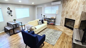 Un salon avec un canapé, un fauteuil bleu, une table basse, une cheminée et un téléviseur.