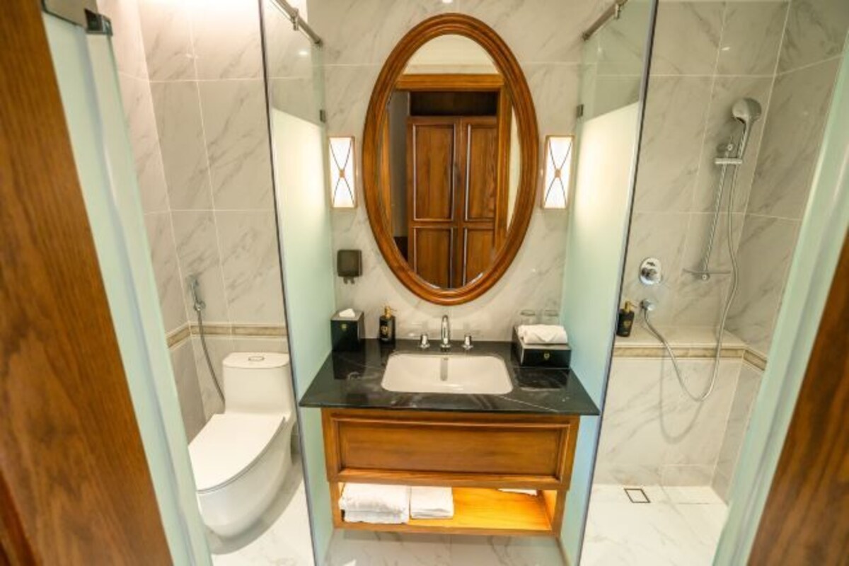 Ein Badezimmer mit Marmorwaschbecken, Holzkommode, einer Duschkabine aus Glas und einer Toilette.