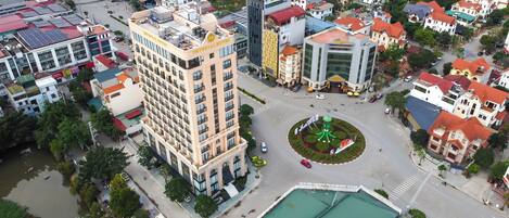 An aerial view of a cityscape with a prominent hotel featuring a central courtyard with a fountain, surrounded by various buildings and streets.