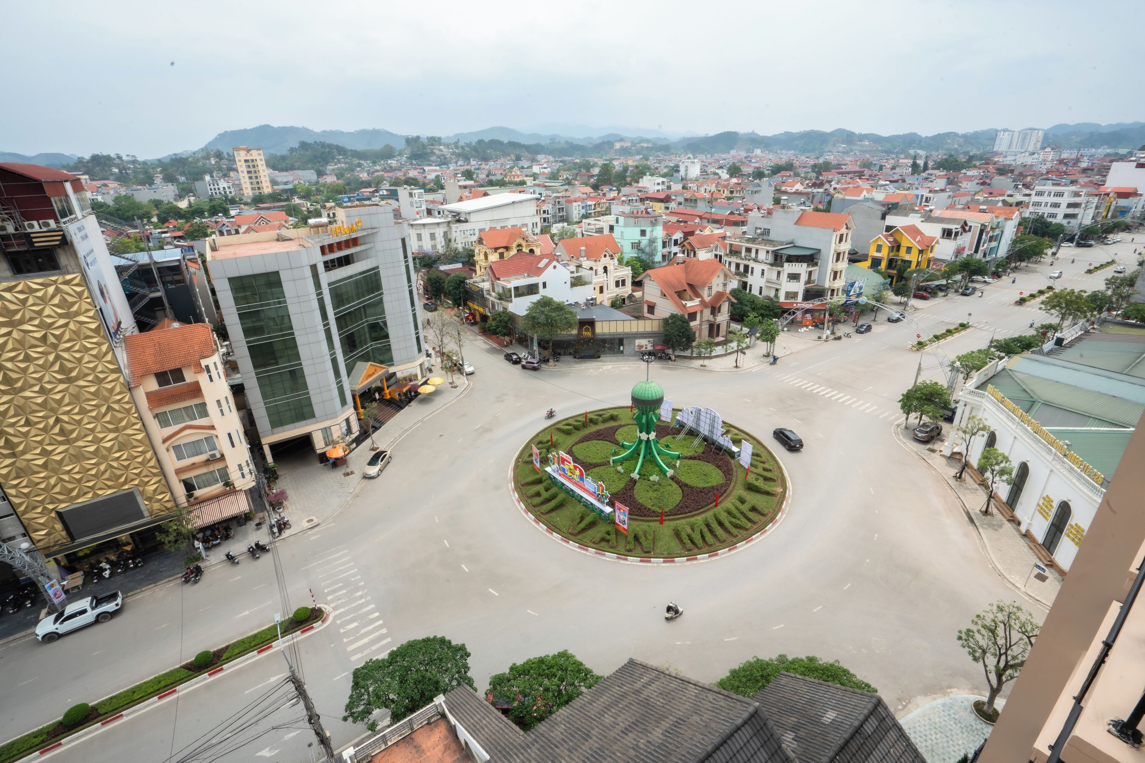 Paisagem urbana com um círculo de rotatórias, edifícios ao redor e uma cadeia montanhosa ao longe.