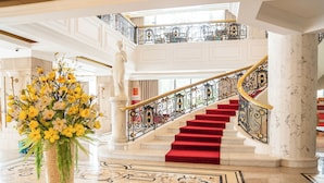 Una imponente escalera con alfombra roja y barandales negros decorativos, que conduce a un piso superior.