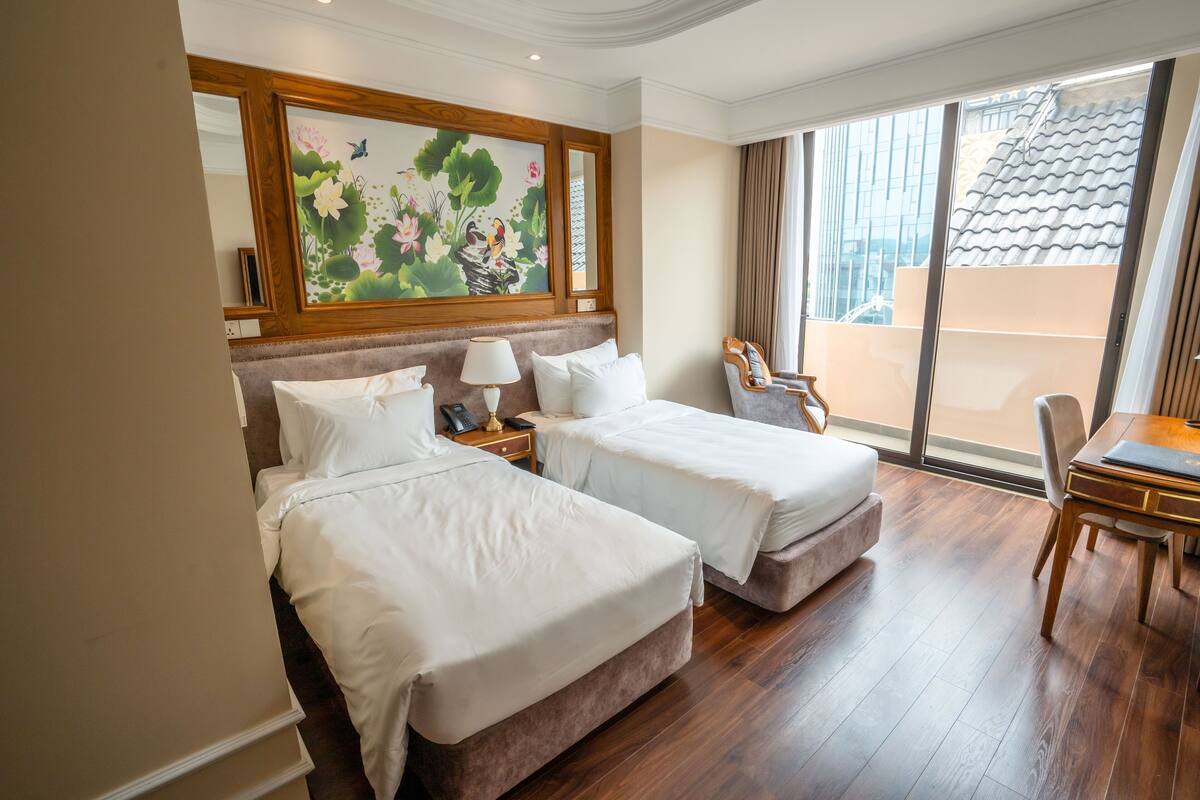 A hotel room with two beds, a dining table, and a large window with a view of a building.
