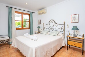Un llit ben arrenjat amb almoiners i tovalloles enrotllades, una taula de nit amb una làmpada, i una finestra amb cortines.