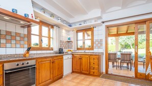 Eine Küche mit Holzausstattung, einem Einbauofen und einem Geschirrspüler. Ein Fenster mit Vorhängen bietet einen Blick ins Freie.