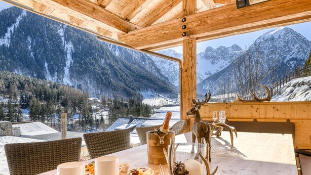 A wooden dining table with a bottle of champagne, a deer head, and a pine cone centerpiece. - Chalet GM - Gardenappartment (Brand)