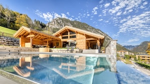 A wooden lodge with a pool, surrounded by mountains and clear skies. - Chalet GM - Gardenappartment (Brand)