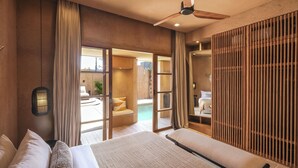 Habitación de hotel moderna con una cama grande, un ventilador de techo y vistas a una piscina al aire libre.