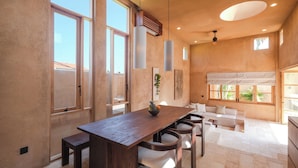 Amplia sala de estar con mesa de comedor de madera, sofá blanco y ventanas grandes que permiten la entrada de luz natural.