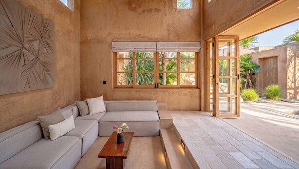Un interior moderno con un sofá modular, una mesa de madera y un ventanal con vistas a la vegetación.