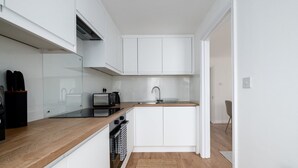 Een compacte keuken met witte kasten, een houten aanrecht, een inbouwoven en een spoelbak.
