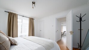 Een slaapkamer met een bed, gordijnen, een kapstok en een deur die leidt naar een eetgedeelte.