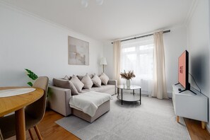 A modern living room with a sofa, a coffee table, a TV, and a dining area.