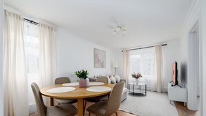 Een moderne woonkamer met een ronde houten eettafel, beige stoelen, een bank en een tv-meubel.