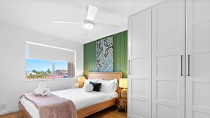 A bedroom with a bed, a window, a ceiling fan, a green accent wall, and a wardrobe. - Azure Walk - Short Walk to the Beach (Scarborough)