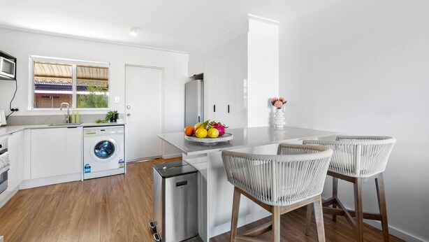 A compact kitchen with a washing machine, a small refrigerator, and a dining area with two wicker chairs. - Azure Walk - Short Walk to the Beach (Scarborough)