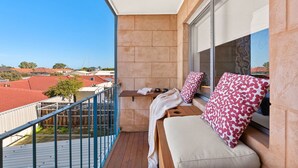 A balcony with a view of red-roofed buildings, a wooden bench, and a window with patterned cushions. - Azure Walk - Short Walk to the Beach (Scarborough)