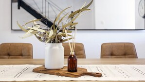 A dining table with a white vase and a brown bottle of reed diffuser, a wooden cutting board, and a placemat. - Terrace Heaven – Luxe Retreat in Fremantle (Fremantle)