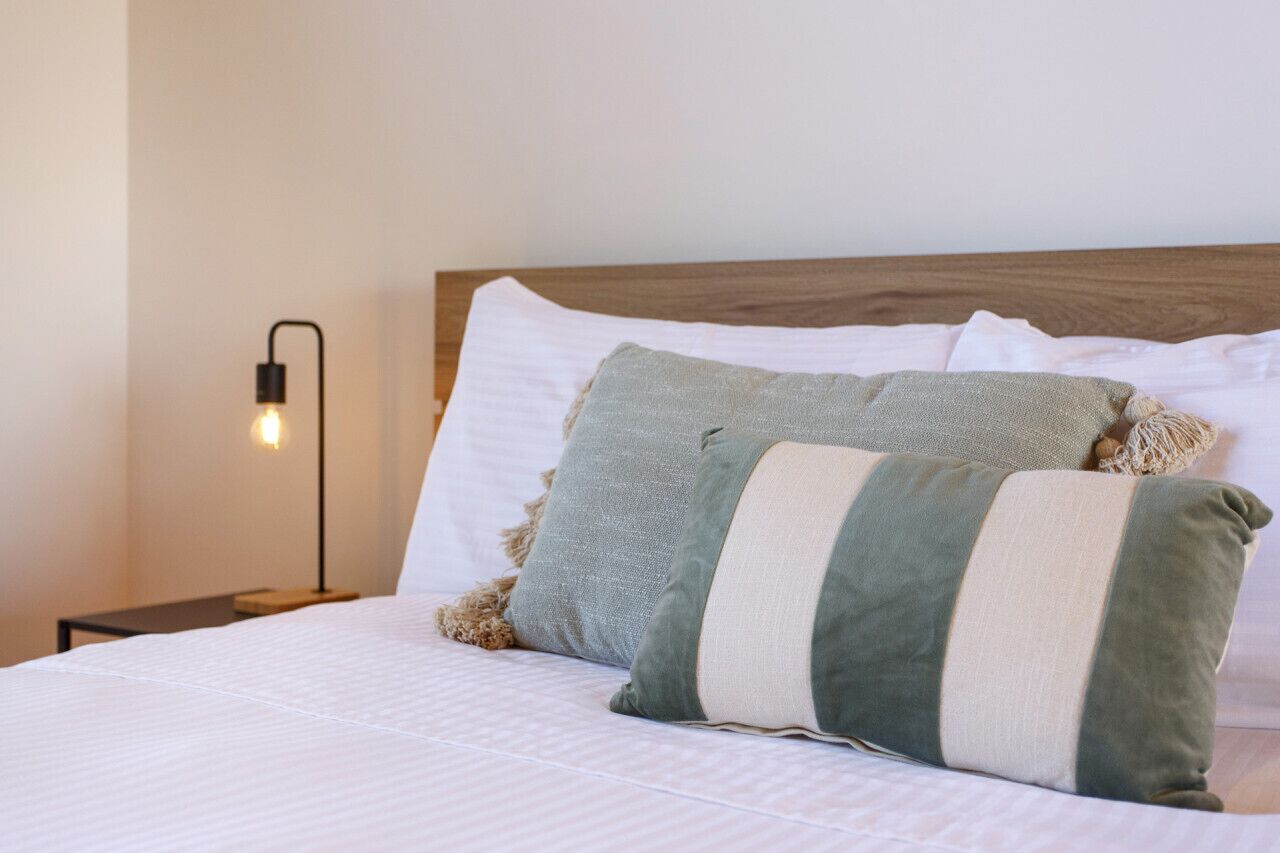 A neatly made bed with white bedding and multiple pillows, including a striped one.