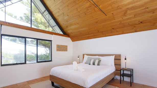 A bedroom with a wooden ceiling, large windows, a bed with white bedding, and a small bedside table with a lamp. - Terrace Heaven – Luxe Retreat in Fremantle (Fremantle)