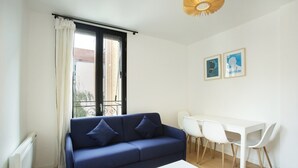 Un salon moderne avec un canapé bleu, une table basse blanche et un coin repas comprenant des chaises blanches et une table blanche.