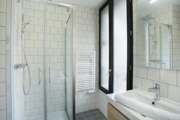 A modern bathroom with a glass-enclosed shower, a white sink, and a large mirror.