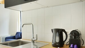 Une cuisine moderne avec un évier en acier inoxydable, une machine à café noire et une bouilloire posée sur le plan de travail.