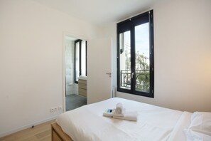 A bedroom with a bed, a window with a view, and a door leading to another room. - Apartement Boulogne Les "passages" (Boulogne-Billancourt)