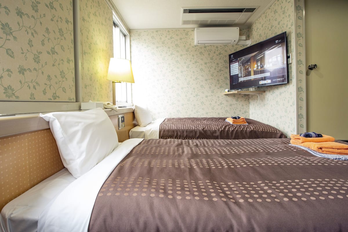 A hotel room with two beds, a TV mounted on the wall, and a window with a view.
