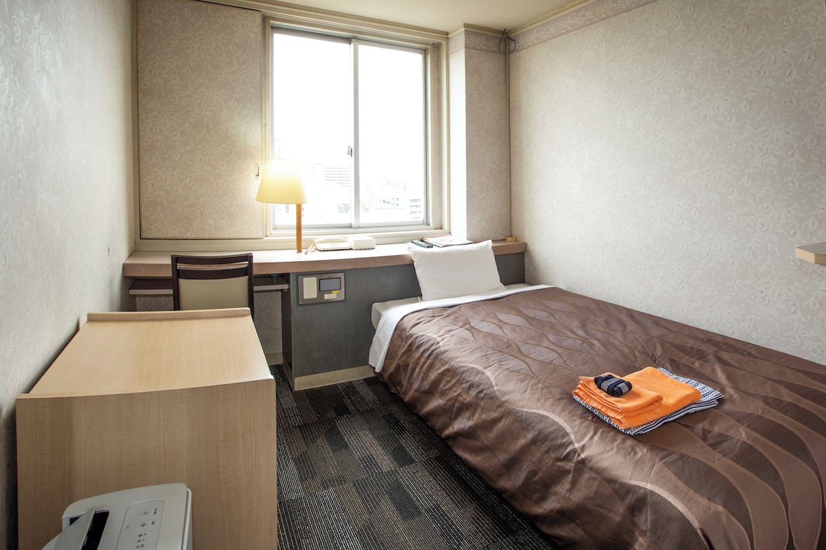 A hotel room with a bed, a desk with a lamp, and a window.