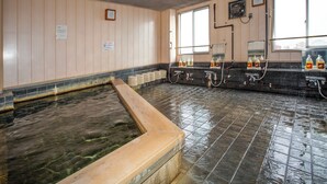 A traditional Japanese onsen with a stone hot spring, tiled walls, and a long bench along the edge.