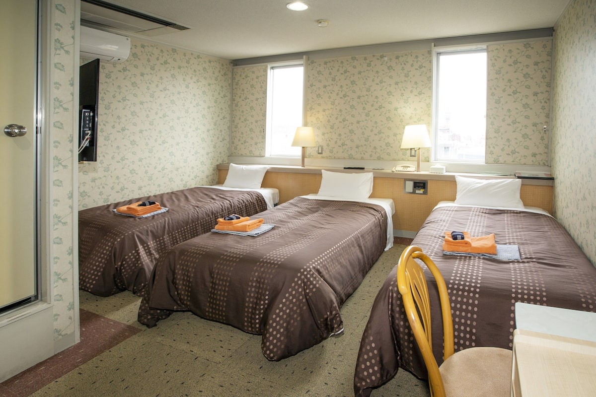 A hotel room with two beds, a desk, a chair, and a window.