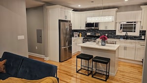 A modern kitchen with white cabinets, a stainless steel refrigerator, a microwave, and a stove. There is a wooden floor, a blue couch, and a yellow throw blanket. - Deluxe Aparment Spacious 3-bedroom apartment with WiFi, AC in nice Elizabeth (Elizabeth)