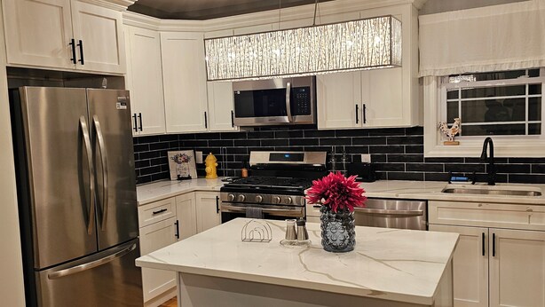A modern kitchen with white cabinets, stainless steel appliances, a central island with stools, and a decorative light fixture. - Deluxe Aparment Spacious 3-bedroom apartment with WiFi, AC in nice Elizabeth (Elizabeth)