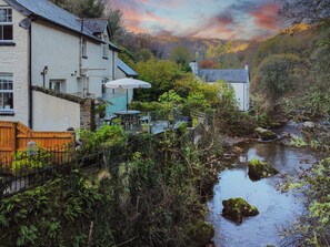 A riverside building with outdoor seating, a staircase, and a view of the surrounding forest. - Rockford Cottage, Brendon (Nr Lynton)