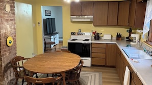 A kitchen with wooden cabinets, a stove, and a dining area with a wooden table and chairs.
