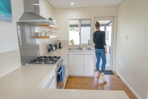 A compact kitchen with a gas stove, a sink, and a window overlooking a garden.