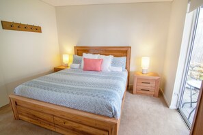 A neatly made bed with a wooden headboard, two bedside tables with lamps, and a view of the outdoors through a large window. - Princess Views in Historic Albany (ALBANY)