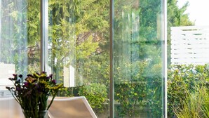 A modern room with a glass table, a vase of flowers, and a view of a lush garden through large windows. - Villa Laurus 4 by Ezoria Villas (Paphos)