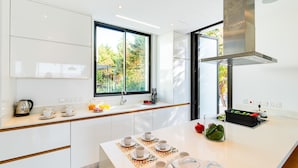 A modern kitchen with white cabinetry, a large window, and a central island with a coffee setup. - Villa Laurus 4 by Ezoria Villas (Paphos)
