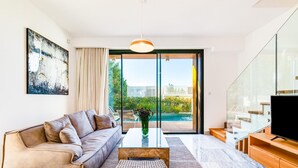 A modern living room with a sofa, coffee table, and TV stand. - Villa Laurus 4 by Ezoria Villas (Paphos)