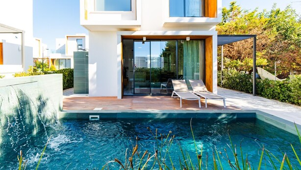 A modern house with a swimming pool, a wooden deck, and a glass door leading to a patio area. - Villa Laurus 4 by Ezoria Villas (Paphos)