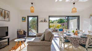 A modern living room with a sofa, a TV, and a dining area with a table set for two. - Azur Cottages by Interhome (Saint Aygulf)