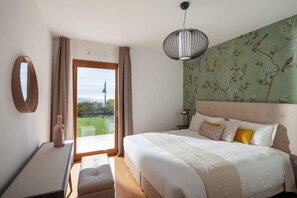 Ein Schlafzimmer mit Bett, Nachttisch, Lampe, Fenster mit Blick und einer Wand mit Blumenmuster.