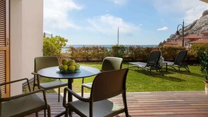 Eine Terrasse mit einem runden Tisch und Stühlen, ein kleiner Garten und Meerblick.
