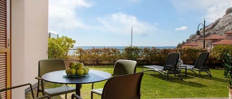 Un patio con una mesa redonda y sillas, un pequeño jardín y vistas al mar.