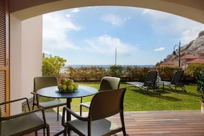 Eine Terrasse mit einem runden Tisch und Stühlen, ein kleiner Garten und Meerblick.