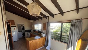Une cuisine compacte avec un îlot central en bois, un four encastré et un évier. On y trouve une fenêtre avec des rideaux, et un ventilateur de plafond est visible.