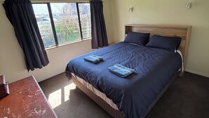 Une chambre à coucher avec un lit, une commode en bois, une fenêtre avec des rideaux et un plafond muni d’un luminaire.