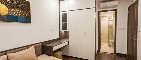 A bedroom with a bed, a desk, wardrobe, and a bathroom visible through an open door.