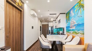 A modern dining area with a white table and chairs, a wooden door, and a mural of a sailboat on the wall. - X-Stay Luxe (Hai Phong)